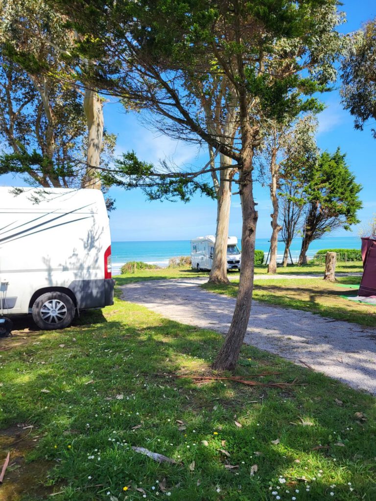 Ein Campingplatz in Nordspanien, zwei weiße Vans, Blick aufs Meer, dazwischen Bäume.
