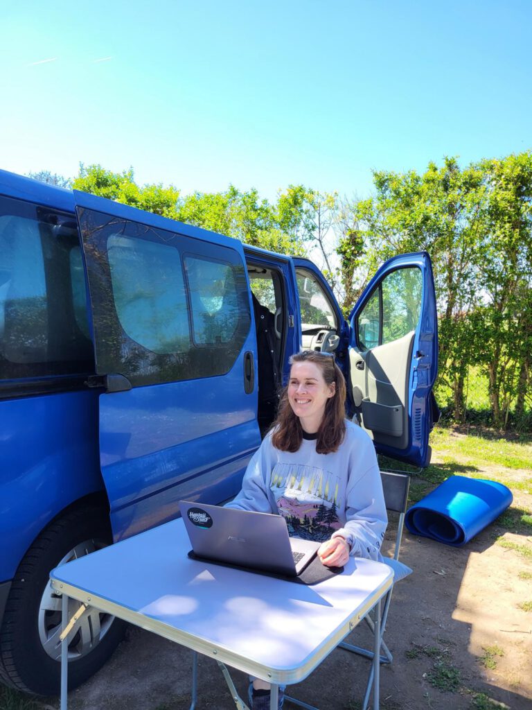 Eine Frau am Laptop vor einem blauen Van.