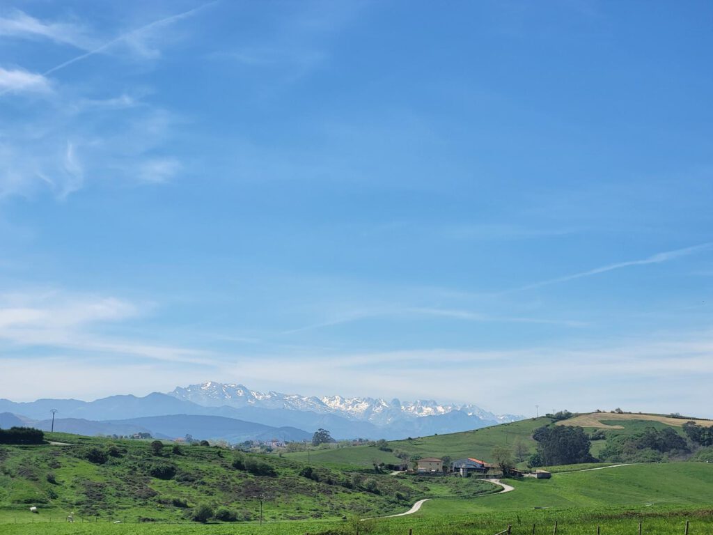 Berglandschaft in Nordspanien, davor grüne hügelige Wiesen, blauer Himmel.
